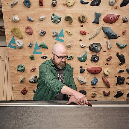 Bild von xelware: Handwerker arbeitet konzentriert an einem Werkst&uuml;ck in seiner Werkstatt vor einer Kletterwand.