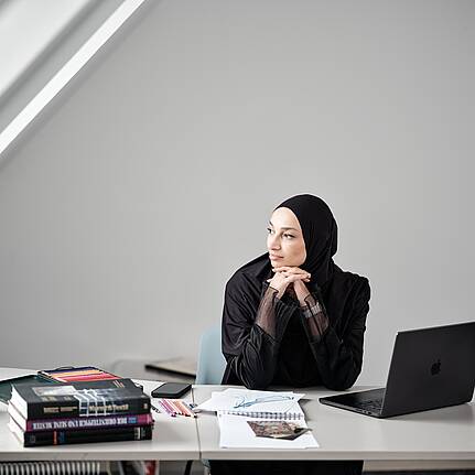 Bild von xelware: Eine Unternehmerin sitzt am Schreibtisch vor ihrem Laptop und schaut nachdenklich aus dem Fenster