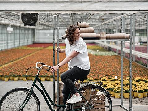 Bild von xelware: Frau sitzt auf Fahrrad vor einem offenen Gewächshaus mit Blumen