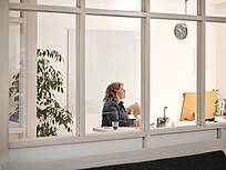 Bild von xelware: Sicht von au&szlig;en durchs Fenster auf eine Unternehmerin am Schreibtisch vorm Bildschirm