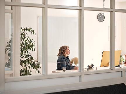 Bild von xelware: Sicht von au&szlig;en durchs Fenster auf eine Unternehmerin am Schreibtisch vorm Bildschirm