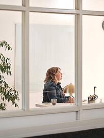 Bild von xelware: Sicht von au&szlig;en durchs Fenster auf eine Unternehmerin am Schreibtisch vorm Bildschirm